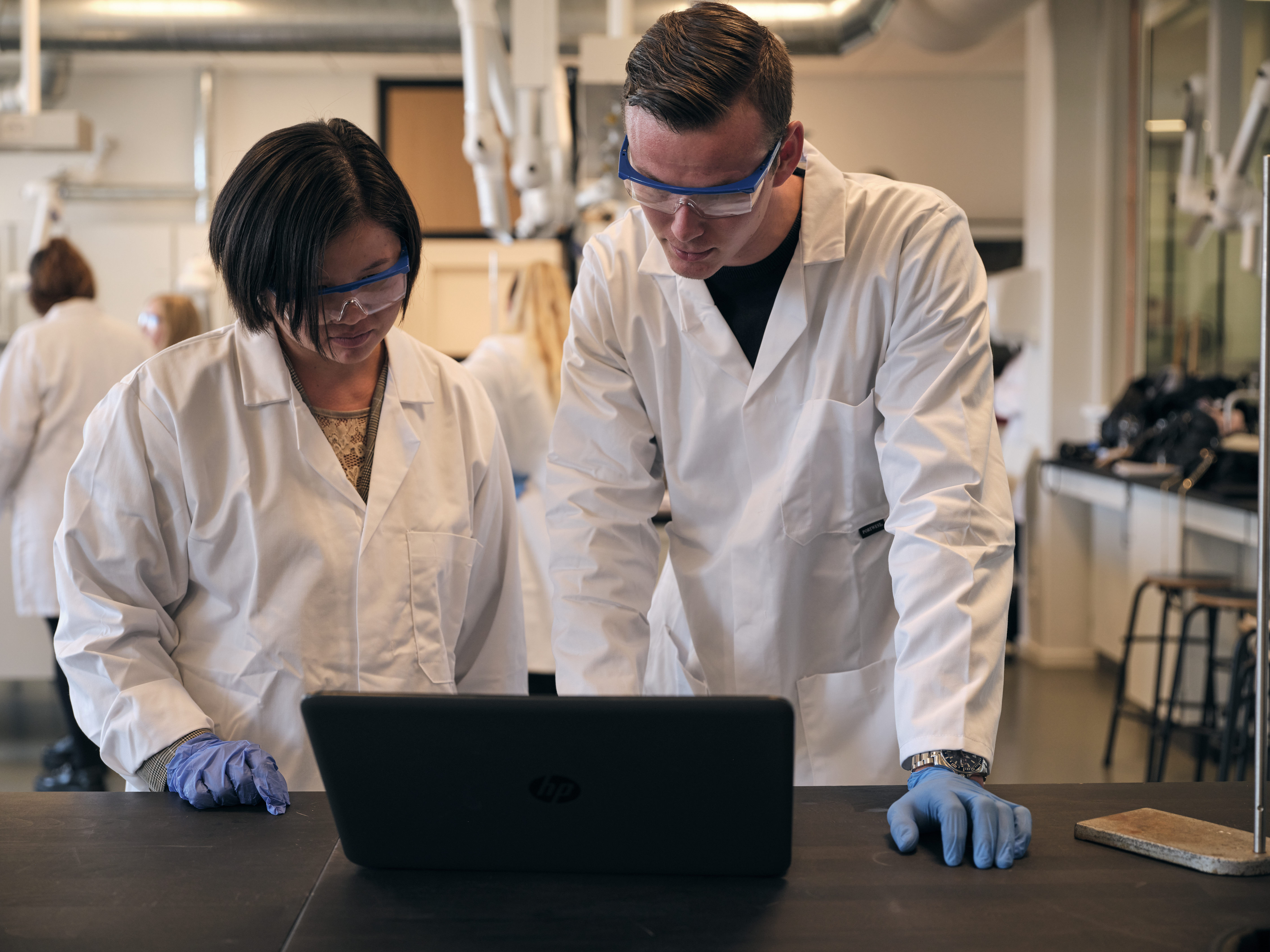 To studerende i kitler foran en computer