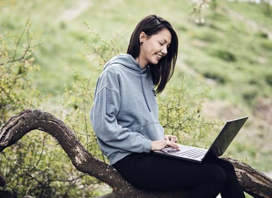 Pige med computer der sidder på en gren